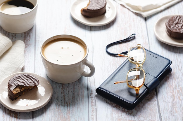 Tazas de café, vasos de alfajores de chocolate y un cuaderno sobre una mesa de madera