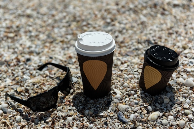 Tazas de café y vasos en la arena a la orilla del mar