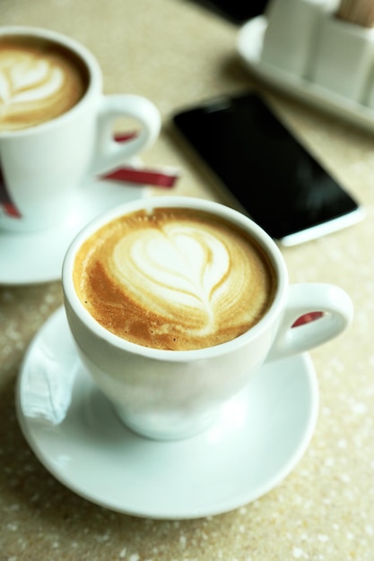 Tazas de capuchino con corazón de espuma en la mesa de café