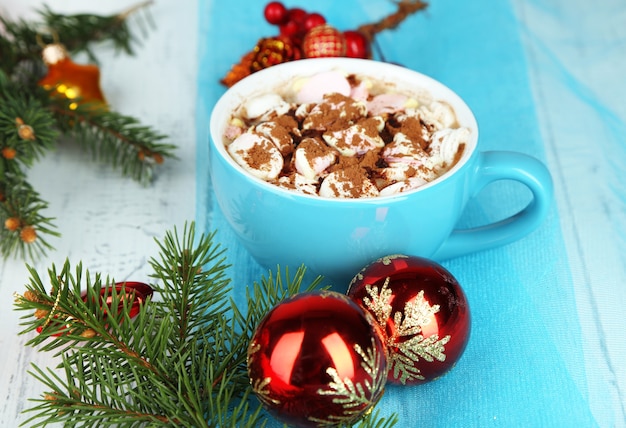 Tazas de chocolate caliente con crema en color, sobre la mesa, sobre fondo de adornos navideños