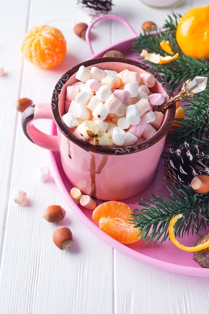 Tazas de chocolate caliente con malvaviscos, mandarina, ramas de abeto y nueces en madera blanca