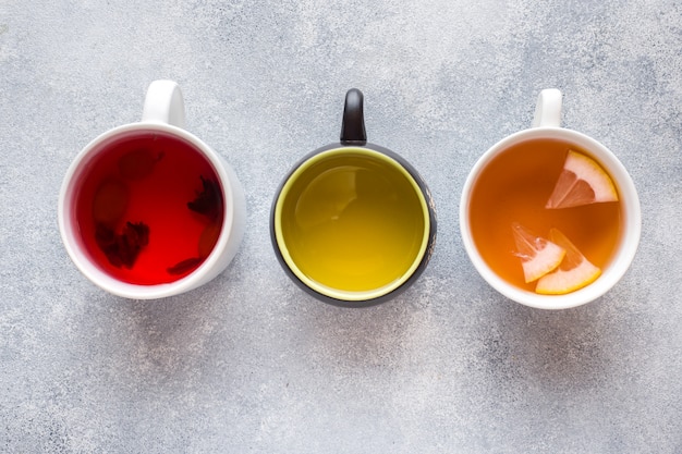 Tazas con diferente té rojo, verde y negro sobre mesa gris
