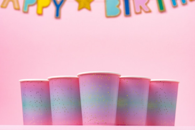 Tazas de fiesta rosa con guirnalda de feliz cumpleaños sobre fondo rosa