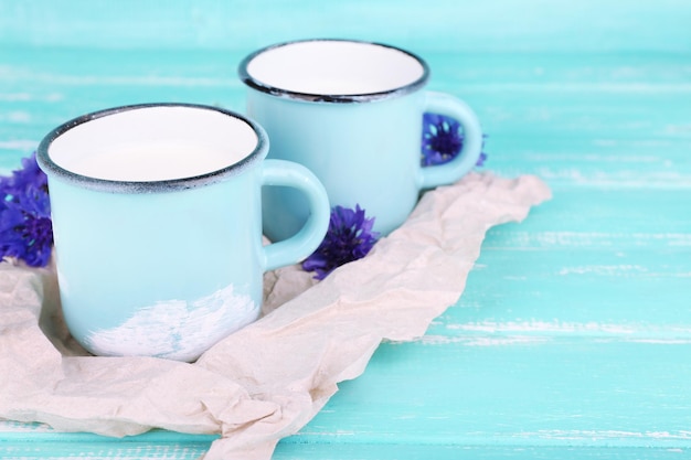 Tazas de leche y acianos en mesa de madera