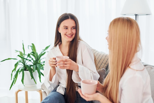 Foto con tazas en las manos la joven madre con su hija está en casa durante el día