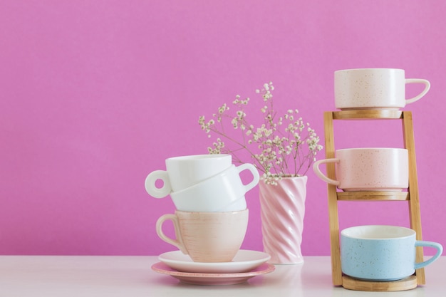 Tazas modernas en mesa blanca en la pared de fondo rosa