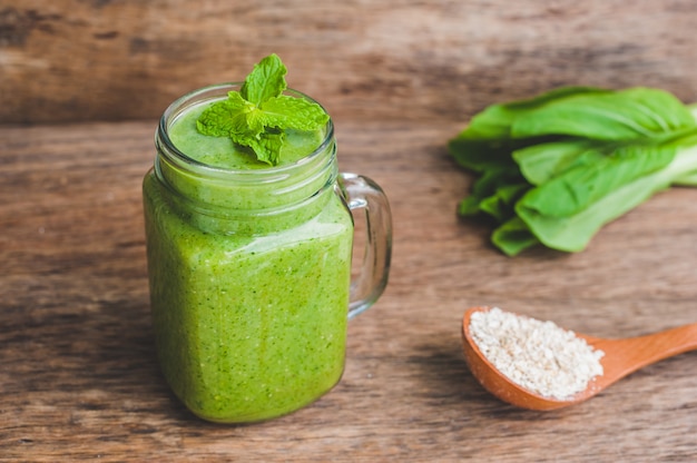 Tazas de tarro de masón llenas de espinacas verdes, plátano y batido de leche de coco con una cuchara de avena en la mesa