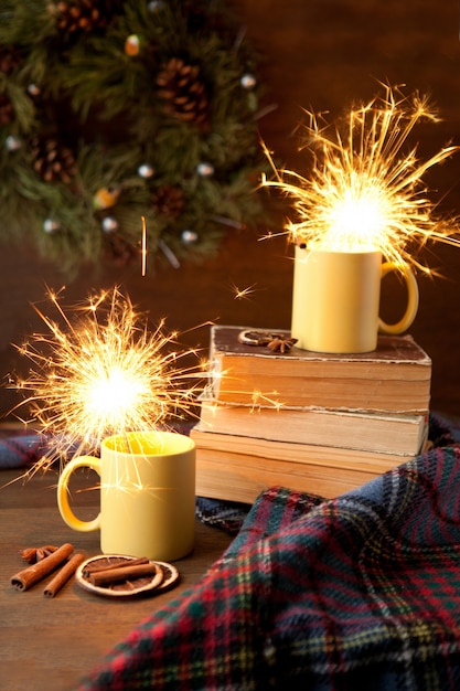 Tazas de té amarillo con brillo y fondo navideño, taza de cerámica con luz brillante en el interior, libros y manta con pergaminos y canela