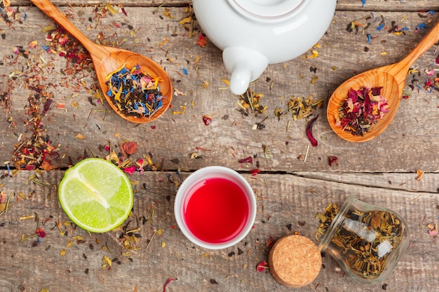 Tazas de té de hierbas saludable con canela, rosa seca y flores de manzanilla en cucharas sobre madera, vista superior