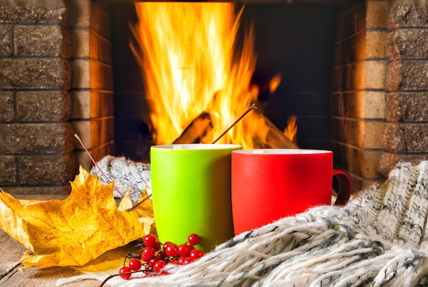 Tazas de té o café y hojas de otoño ante la acogedora chimenea.