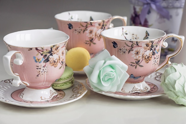 Tazas de té rosa con adornos florales y dulces de macarrón