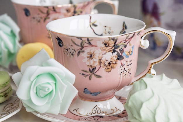 Tazas de té rosa con adornos florales y dulces de macarrón