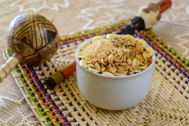 Tazón de acai brasileño con maní de granola y plátano en una mesa con artesanías de la región amazónica borrosas en el fondo