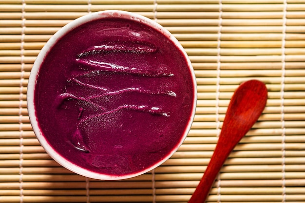 Foto tazón de acai en un mantel de bambú con una cuchara al lado.