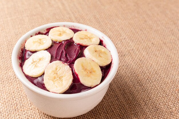 Foto tazón de acai con plátano y cereal en tela de arpillera.