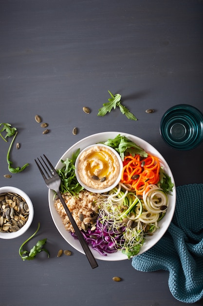 Tazón de almuerzo de cuscús vegetariano con zanahorias espiraladas y calabacín, hummus y col roja