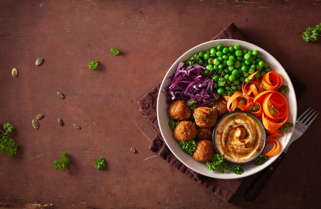 Tazón de almuerzo vegano saludable con falafel hummus zanahoria cintas repollo y guisantes