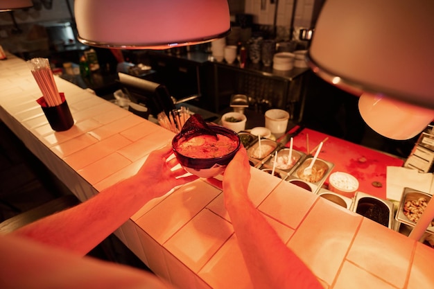 Tazón con apetitoso ramen en manos de un joven sosteniendo comida sobre el mostrador