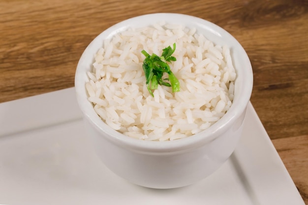 Un tazón de arroz blanco cocinado en un tazón blanco sobre un fondo de madera