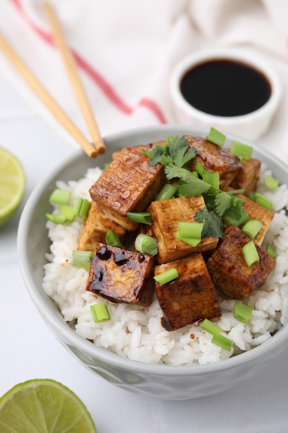Tazón de arroz con tofu frito y verduras en primer plano de la mesa de azulejos blancos