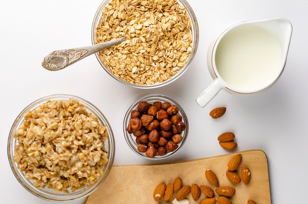 Tazón de avena arrollada, gachas de avena, leche, avellanas y almendras sobre tabla de madera