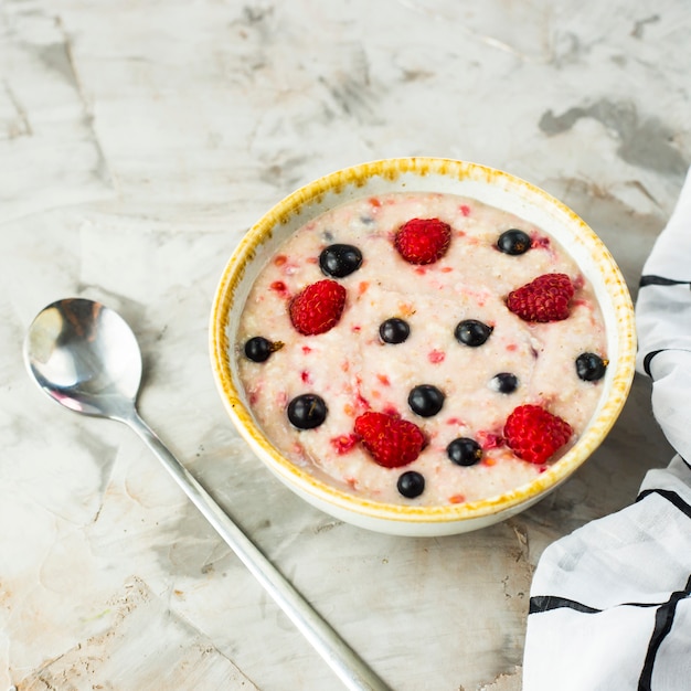 Un tazón de avena con frambuesas y arándanos en una mesa gris