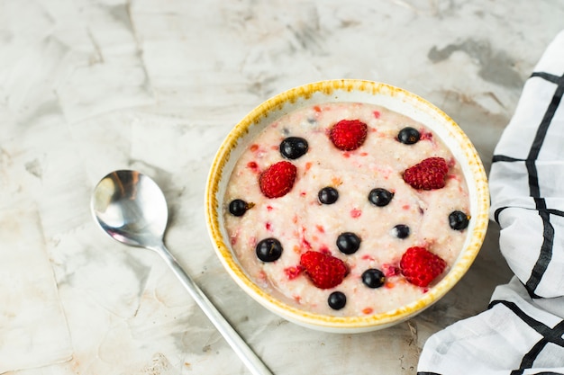 Un tazón de avena con frambuesas y arándanos en una mesa gris