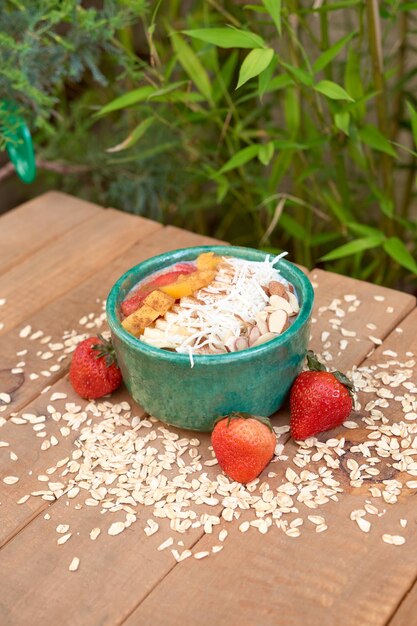 Tazón de avena con granola de fresa, almendras de coco tostadas y melocotones sobre una mesa de madera