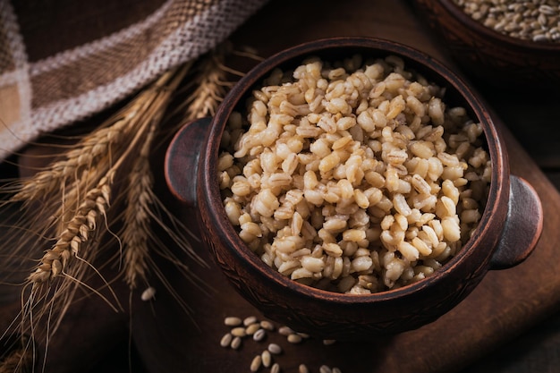 Tazón de avena de granos de cebada pelados cocidos con espigas de trigo sobre fondo de madera oscura Concepto de comida saludable y dietética para cocinar