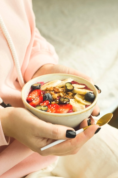 Tazón de batido de alimentos saludables con bayas y granola en manos de la mujer.