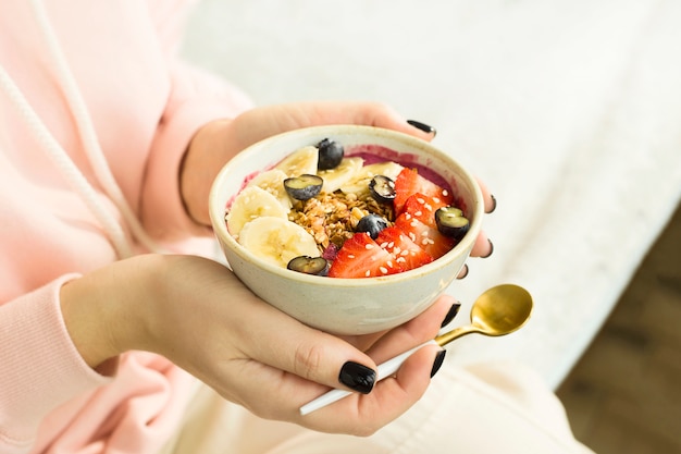 Tazón de batido de alimentos saludables con bayas y granola en manos de la mujer.