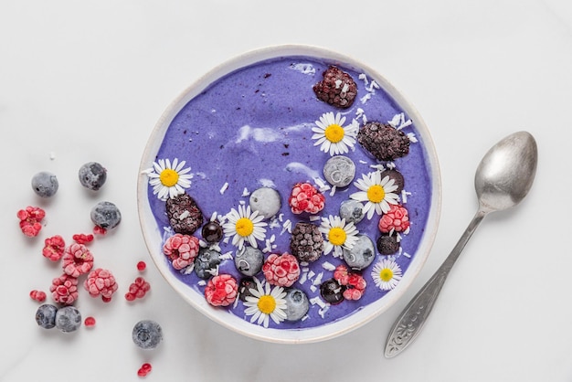 Tazón de batido con bayas congeladas y flores sobre fondo blanco Muy Peri color del año 2022 vista superior desayuno saludable