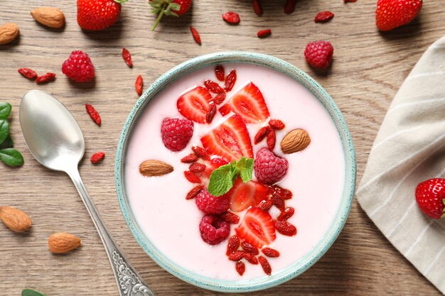 Tazón de batido con bayas de goji y cuchara en la mesa de madera plana