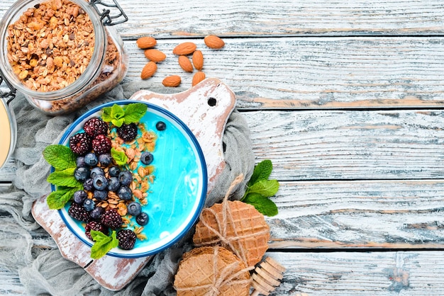 Tazón de batido de espirulina azul y frutas frescas Cubierto con moras, arándanos, granola y yogur. Desayuno. Vista superior. Espacio libre para su texto.