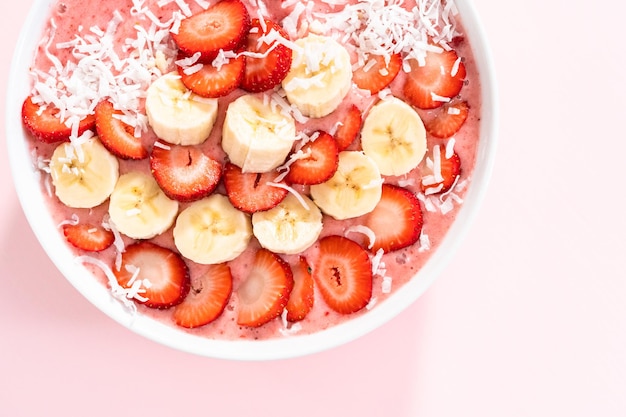 Tazón de batido de fresa y plátano adornado con copos de coco y frutas frescas.