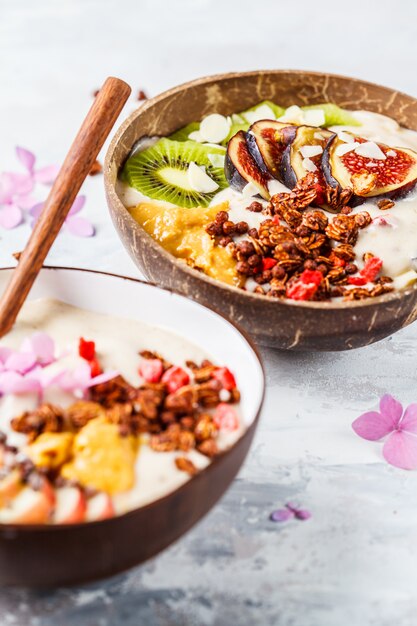 Tazón de batido con frutas y granola con tazón de cáscara de coco sobre fondo gris Comida vegana saludable.