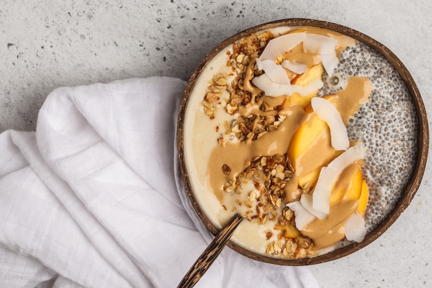 Un tazón de batido con pudín de chia, melocotón, coco y granola en un tazón de coco. desayuno saludable vegano, concepto de alimentación limpia.