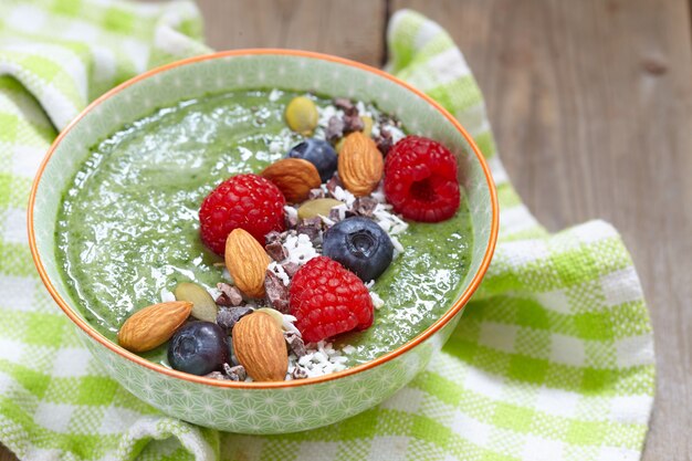 Tazón de batido verde con cobertura de frutos secos, frutos secos y semillas