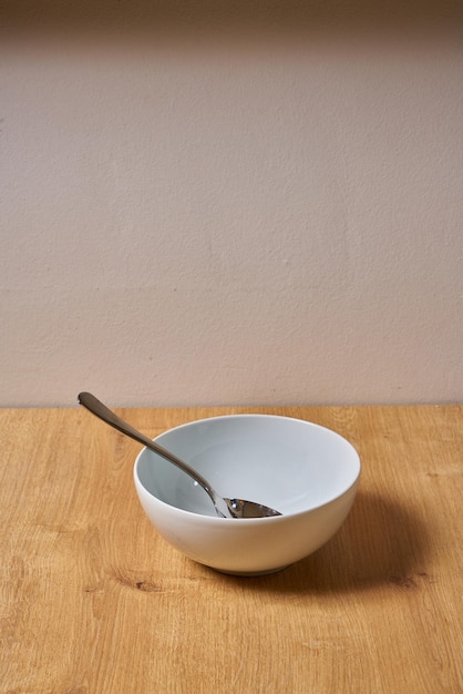 Un tazón blanco con una cuchara se sienta sobre una mesa de madera.