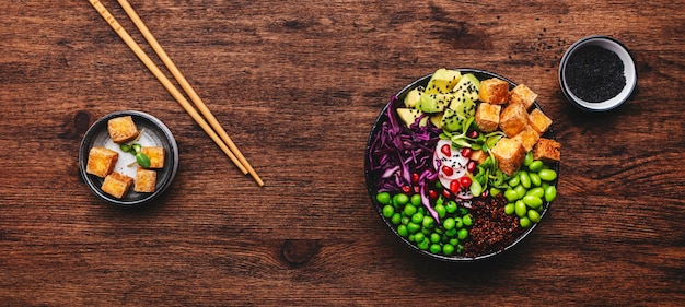 Tazón de buda vegetariano vegano con tofu frito con quinua, aguacate, frijoles edamame, guisantes, rábano, repollo rojo y semillas de sésamo. Comida de dieta saludable. Fondo de mesa de cocina de madera.