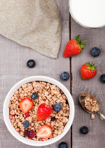 Tazón de cereal saludable granola con fresas y arándanos y vaso de leche sobre tabla de madera