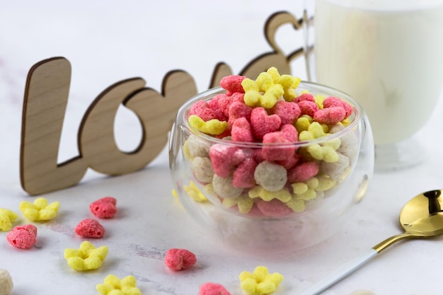 Un tazón de cereales para el desayuno, un vaso de leche y una inscripción de amor de madera sobre una mesa blanca Desayuno romántico