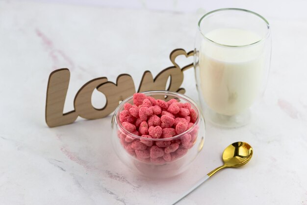 Un tazón de cereales para el desayuno, un vaso de leche y una inscripción de amor de madera sobre una mesa blanca Desayuno romántico