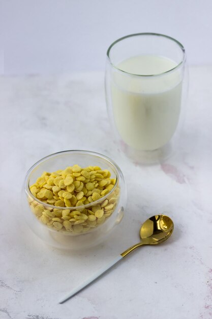 Un tazón de cereales para el desayuno y un vaso de leche sobre una mesa de mármol blanco Copos de maíz instantáneos