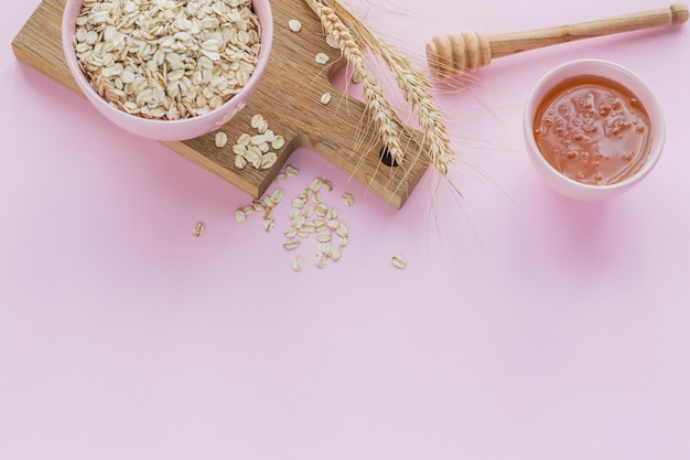 Tazón de copos de avena secos con espigas de trigo sobre fondo claro