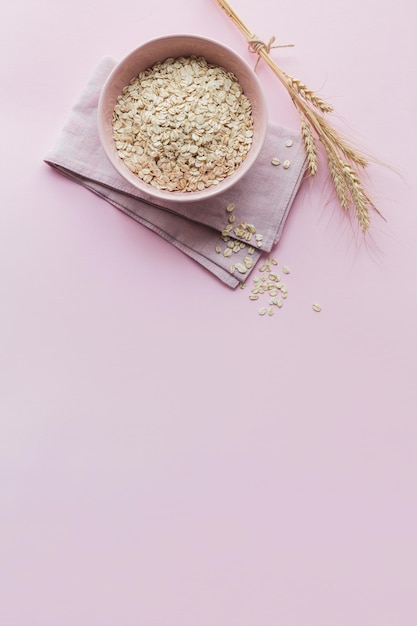 Tazón de copos de avena secos con espigas de trigo sobre fondo rosa claro