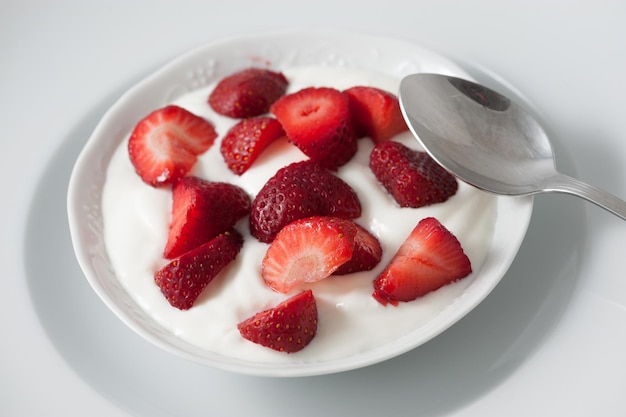 Tazón y cuchara de porcelana con fresas y crema de yogur