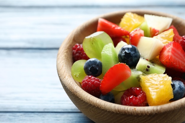 Tazón con deliciosa ensalada de frutas sobre fondo de madera