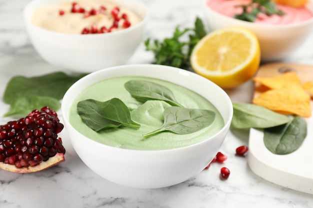 Tazón de delicioso hummus verde con espinacas sobre mesa de mármol blanco