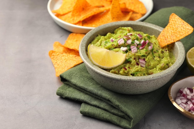 Tazón de deliciosos chips de nachos de guacamole y lima en el primer plano de la mesa gris Espacio para texto